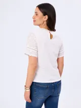 Blusa blanca de algodón con delicados bordados florales, cuello redondo y mangas cortas. Presenta detalles de calados geométricos en las costuras y aberturas laterales en el dobladillo.