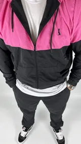 Campera deportiva con capucha, combinada en fucsia y negro, con cierre frontal y bolsillos laterales.