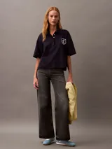 Chomba azul marino de punto de algodón con cuello clásico, tapeta con botones ocultos y mangas cortas. Presenta un corte holgado y un escudo bordado con el logo de Calvin Klein en el pecho.