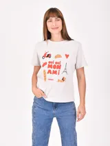 Remera lila de corte recto y mangas cortas, con estampado pequeño de un gato blanco con gorro rojo, gafas de sol y copa de vino, junto a la frase 'J'adore'.