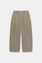 Pantalón fluido de tiro medio color verde militar, con cintura elástica en la parte trasera, pinzas en el delantero y bolsillos laterales ocultos en la costura. Presenta un diseño de pernera ancha y corte tobillero, con cierre frontal de cremallera y botón.