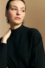 Polera de cuello alto confeccionada en tejido de punto negro, con diseño de textura acanalada en cuello, puños y ruedo, y trama vertical en mangas y espalda.