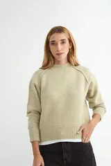 Buzo de tejido de punto color beige, con cuello redondo alto, mangas largas con costuras raglán y puños y ruedo acanalados.