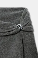 Jersey de punto color gris oscuro, con escote recto tipo off-shoulder, manga larga y detalle de aplique metálico en el hombro. Presenta acabados en rib en puños y ruedo.