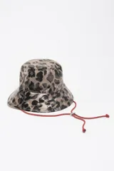 Gorro bucket de poliuretano termoplástico con estampado animal print en tonos beige y negro, y cordón ajustable rojo con traba metálica.