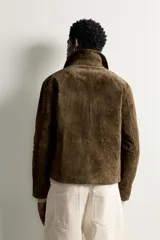 Sobrecamisa regular fit confeccionada en piel con acabado serraje de color marrón oscuro, con cuello solapa, bolsillos de vivo en la cadera y cierre frontal con cremallera.