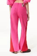 Pantalón de jean fucsia de pierna ancha con corte lateral acordonado en el bajo y detalle de tela roja en el lateral.