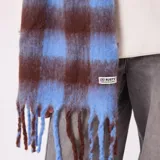 Bufanda de tejido suave con diseño de cuadros grandes en tonos azul y marrón, con flecos en los extremos y etiqueta de la marca Rusty.