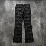 Pantalón de denim negro con acabado encerado, corte acampanado y diseño decorado con rombos formados por pedrería brillante en toda la superficie.