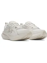 Championes Under Armour modelo W Assert 11, de color blanco y tiza, diseñados para running y entrenamiento. Presentan una capellada de malla transpirable con superposiciones de cuero resistente, mediasuela con amortiguación Charged+ Cushioning y suela exterior de goma.