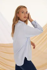 Camisa verde militar de corte holgado, con cuello clásico, cierre frontal con botones, bolsillo de parche en el pecho y mangas largas con puños abotonados.