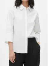 Camisa blanca de algodón con corte holgado (loose fit), cuello clásico y mangas amplias de tres cuartos con puños anchos.