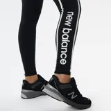 Calza larga negra de New Balance con cintura alta, corte ajustado y logo estampado en la pierna. Presenta una banda lateral blanca con el logo de la marca.