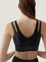 Top deportivo negro de sujeción media-alta, con escote en V y tirantes dobles en los hombros. Presenta paneles centrales con textura acanalada y una banda ancha inferior.