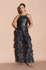 Pantalón negro brillante con volados en capas a lo largo de las piernas, de corte recto y tiro alto.