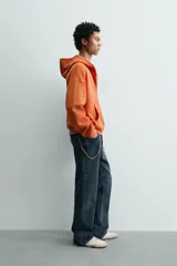 Sudadera tipo hoodie de corte relajado, confeccionada en tejido de algodón con textura estructurada y efecto lavado. Presenta cierre frontal con cremallera, cuello con capucha, manga larga, bolsillos tipo canguro y acabados en rib.