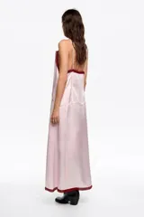 Vestido midi de corte recto confeccionado en una mezcla de acetato y viscosa. Presenta escote en pico con detalles de encaje, tirantes finos y un lazo decorativo en el centro del pecho. El diseño incluye tiras cosidas a lo largo de la prenda que aportan textura.