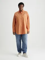 Camisa color naranja de algodón con corte holgado, cuello clásico, cierre frontal con botones y logo bordado en el pecho.