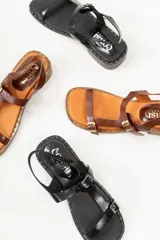 Sandalias negras de cuero con diseño de tiras rectas, hebillas metálicas y un mini taco de 1.5 cm. La suela tiene detalles de tachas pequeñas.