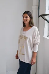 Remera de corte holgado y mangas largas, color beige, con estampado floral en tonos dorados en la parte frontal.