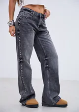 Jean de corte recto y tiro medio, confeccionado en denim gris con efecto lavado. Presenta una hilera de tachas metálicas pequeñas a lo largo de la costura lateral externa de ambas piernas.