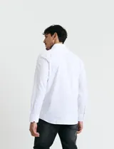 Camisa de vestir blanca de manga larga, con cuello clásico y cierre frontal de botones.