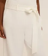 Pantalón de sastrería modelo pantalona color blanco, de corte ancho y recto, con cintura elástica con trabillas, bolsillos laterales y un cinturón de lazo ajustable en la misma tela.