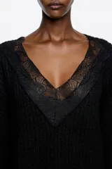 Jersey largo de punto negro con escote en V profundo adornado con detalles de encaje. Presenta mangas largas con puños ajustados y un diseño de tejido acanalado.