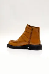 Bota corta color marrón de cuero, con puntera redondeada, suela de goma negra y cierre con cremallera lateral y doble hebilla.