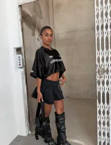 Minifalda de tiro bajo confeccionada en denim negro, con diseño plisado y detalle de hebilla frontal. Presenta un tajo lateral que aporta un estilo moderno y audaz.