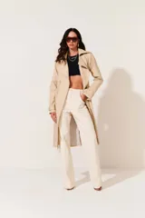 Trench color beige, con cuello solapa, doble botonadura frontal, cinturón y bolsillos laterales.