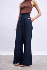 Pantalon de vestir de corte recto y tiro alto, confeccionado en tela de lino en color beige. Presenta pinzas frontales, cierre con botón y detalle de vivos en contraste en la cintura.