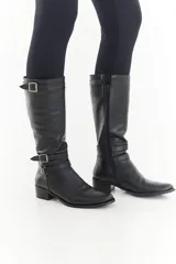 Bota de caña alta de cuero liso negro, con diseño clásico, detalles de hebillas metálicas, cierre lateral y taco bajo.