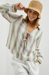 Blusa de lino a rayas verticales de color blanco, naranja, verde y marrón, con cuello camisero, mangas largas con puños y lazos ajustables en el escote.