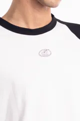 Remera de corte oversize con diseño tipo ranglan, que combina cuerpo blanco con mangas y cuello en color negro. Presenta un pequeño logo bordado en el centro del pecho.