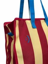 Bolso tote con rayas horizontales rojas y amarillas, asas de mano azules y cierre superior con cremallera.