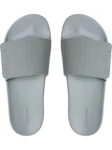 Ojotas tipo slide de color gris claro, con base de EVA moldeada ergonómicamente con soporte para el arco plantar. La tira superior es de lona de algodón reciclado con la marca Calvin Klein grabada en relieve en los laterales.