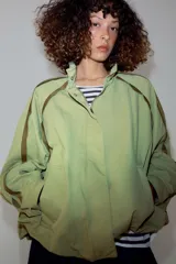 Cazadora ZARA Woman Collection color verde militar, con cuello alto, manga larga y bolsillos frontales. Cuenta con detalles de vivos a contraste en los hombros, bajo elástico asimétrico y cierre frontal oculto con cremallera y botones.