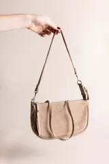 Cartera tipo bandolera de gamuza en color tostado, con diseño rectangular y bordes redondeados. Cuenta con cierre superior, una correa larga ajustable y una correa corta de mano.