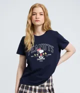 Remera de algodón color azul marino con cuello redondo y mangas cortas. Presenta un estampado frontal con el personaje Snoopy jugando al golf y la inscripción Peanuts Golf Champion 1986.