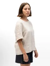 Remera de lino con corte holgado, cuello redondo y mangas cortas. Presenta un diseño minimalista con detalle de botones en la espalda.