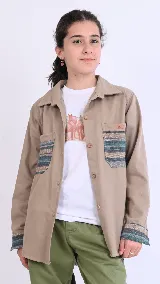 Sobre camisa beige de manga larga, con bolsillos en el pecho y detalles de tela guardamonte en los bolsillos y puños.