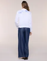 Campera liviana de lino color blanco, con estilo denim y silueta semi entallada. Presenta un canesú superior estampado con motivos florales en tonos azules y tostados, cuello camisero, abotonadura frontal con botones rústicos y bolsillos con solapa en el pecho.
