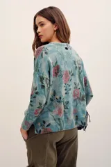 Sweater de punto con estampado floral en tonos rosados sobre base verde, cuello redondo y mangas largas.