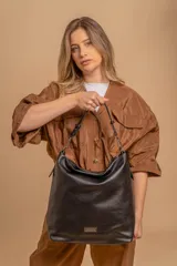 Cartera tipo hobo de gran capacidad, confeccionada en cuero sintético con textura granulada. Presenta un diseño amplio con asa corta ajustable mediante hebillas metálicas y cierre principal. Incluye una placa metálica decorativa en la parte inferior frontal.