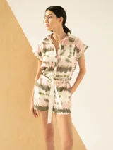 Mono corto con estampado tie-dye en tonos rosa, blanco y verde. Presenta cuello camisero, mangas cortas con dobladillo, cierre frontal con botones y cinturón de lazo.