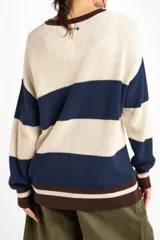 Sweater oversize de tejido de punto con diseño de rayas horizontales anchas en color beige y azul marino, cuello redondo marrón y puños y dobladillo en marrón con líneas beige y blancas.