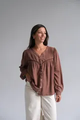 Blusa de color chocolate con cuello en V, cierre frontal con botones y mangas largas abullonadas. Presenta detalles de tablas en la parte superior y una costura horizontal con encaje decorativo en el pecho.