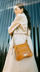 Bandolera color marrón con apertura superior de cierre metálico y dos bolsillos frontales con cierre. Incluye correa larga regulable y placa metálica con el logo de la marca.