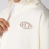 Camisa de manga corta color marfil, corte boxy, con cuello camisero, cierre frontal de botones y pequeño bordado marrón en el pecho con las siglas VCP.